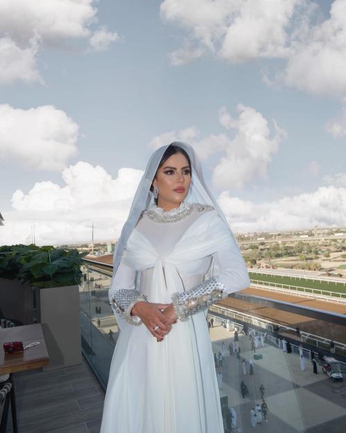 Woman in white abaya on balcony overlooking racetrack.