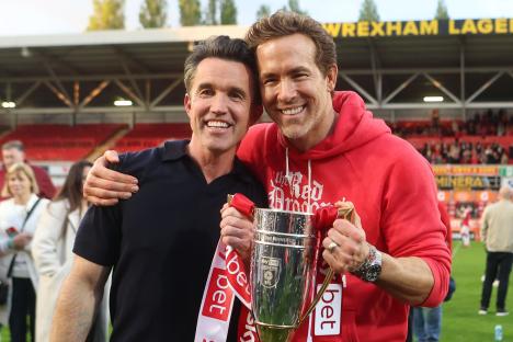 Rob McElhenney and Ryan Reynolds celebrating Wrexham's promotion with a trophy.
