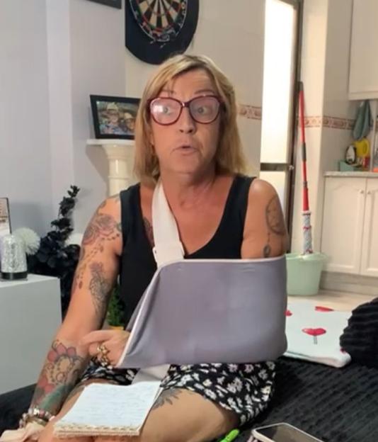 Woman with arm in sling sits on couch and holds notepad.