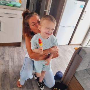 A woman kisses a young boy holding a popsicle.