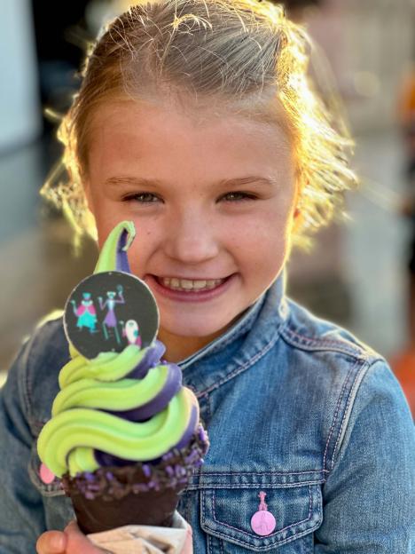 A young child smiling and holding a lime green and purple soft-serve ice cream cone.