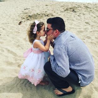 Father and daughter kissing on a beach.
