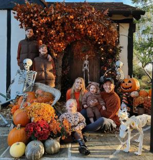 Family in Halloween costumes posing with pumpkins and skeletons.