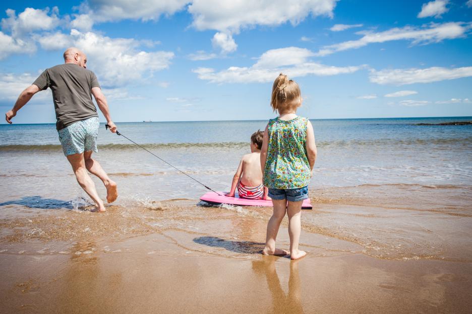 Father pulling his son on a bodyboard in the ocean.