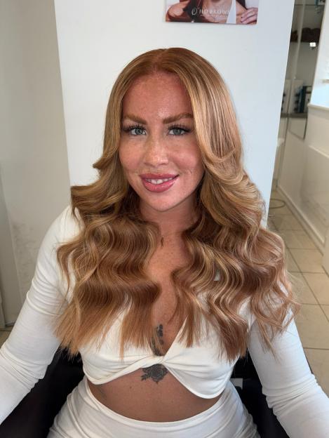 A young woman with long, wavy blonde hair and a white top.