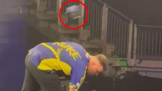 A person in a blue and yellow shirt bending down, picking up something that fell down the stairs.