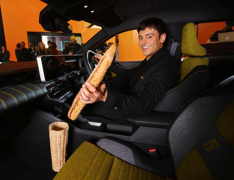 Tom Daley smiling while sitting in a car with a baguette in a basket.
