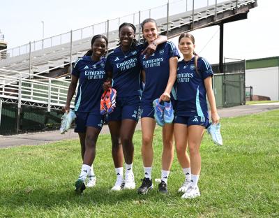 Four Arsenal Women's soccer players holding their cleats.