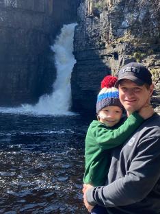 A father and daughter hug in front of a waterfall.