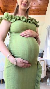 Pregnant person in a green dress cradling their belly.