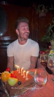 David Beckham smiling at a birthday cake with lit candles.