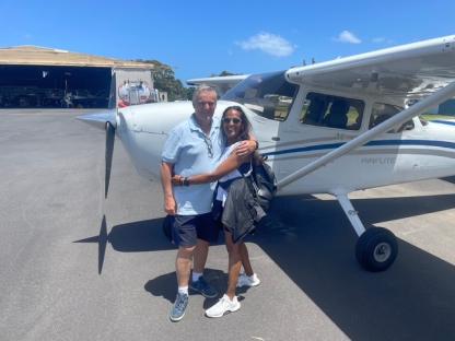 Couple hugging in front of a small airplane.