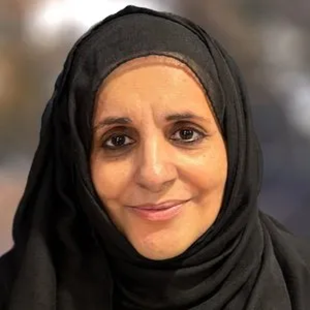 A woman in a black hijab smiles softly at the viewer.
