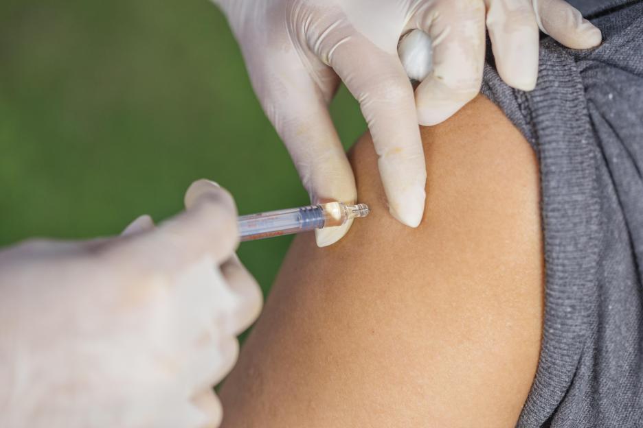 A gloved hand administering a vaccine into a patient's arm.