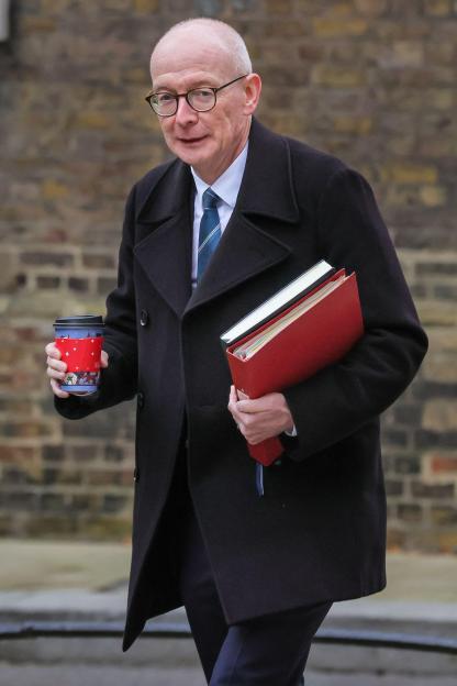 Pat McFadden, Secretary of State for Work and Pensions, MP for Wolverhampton South East, wearing glasses and a dark coat, holding a coffee cup and red folders.