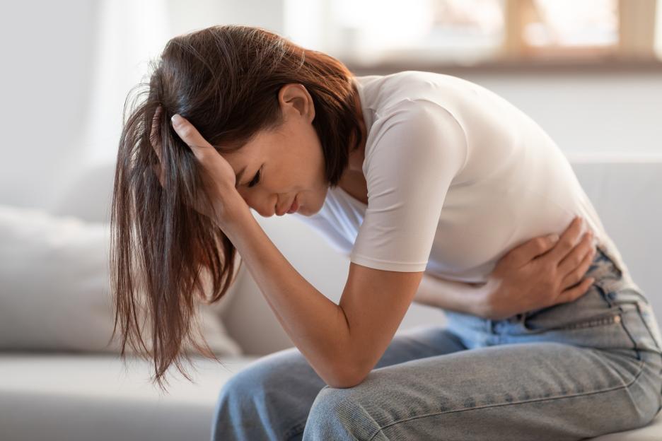 Woman in a white shirt and jeans touching her head and stomach in distress.