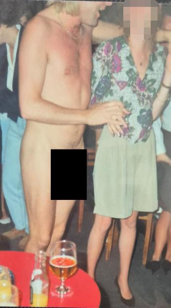 A man, nude and censored, stands next to a woman in a floral shirt and skirt.