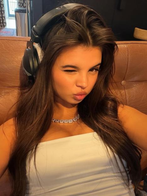 Scarlett Thomas winks at the camera while wearing headphones and a white top.