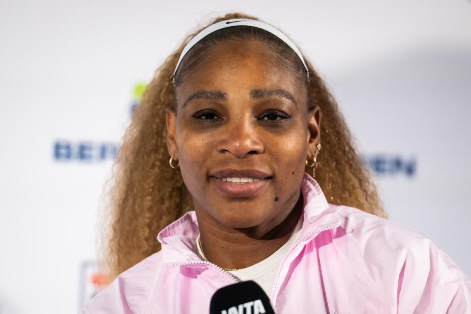 Serena Williams wearing a white headband and pink jacket.