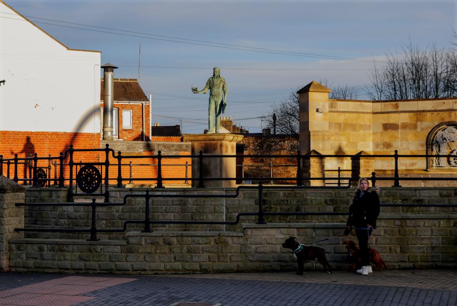 A woman walks two dogs in front of a monument in Shildon, UK.