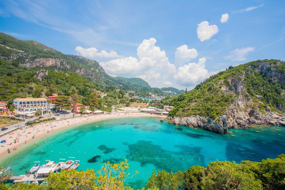 Overview of Corfu Island, Greece with a sandy beach and turquoise waters in a bay surrounded by green hills.
