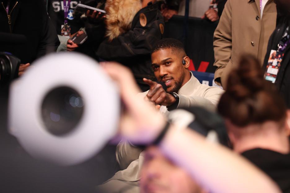 Anthony Joshua, wearing an earpiece, speaks to someone off-camera and points his finger.