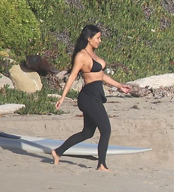 Kim Kardashian in a black bikini top and black leggings on a beach.