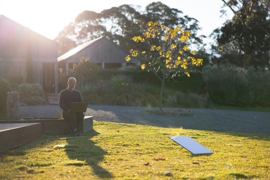 A man using a laptop outdoors with a Starlink dish visible on the lawn.