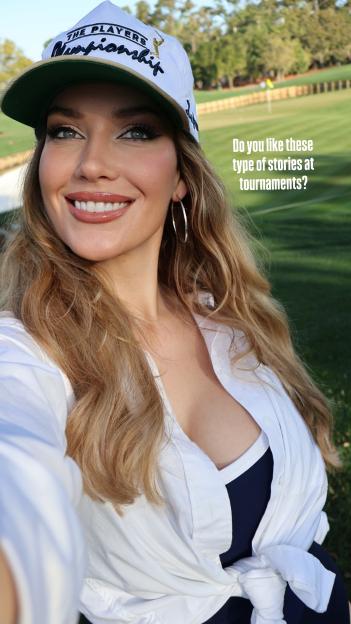 Paige Spiranac smiling in a white hat and shirt at a golf course.