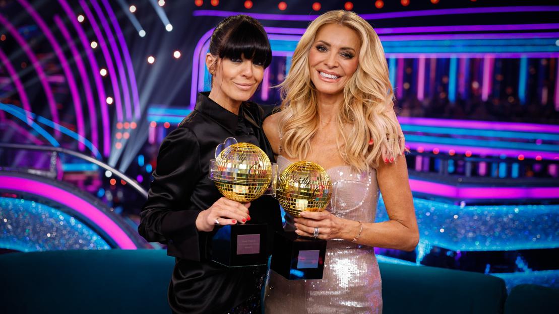 Claudia Winkleman and Tess Daly holding golden disco ball trophies.