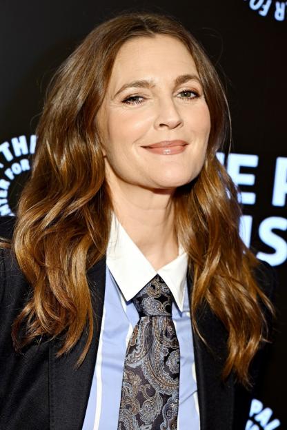 Drew Barrymore smiles at the "Daytime at Night" event, wearing a black blazer, light blue striped shirt, and patterned tie.