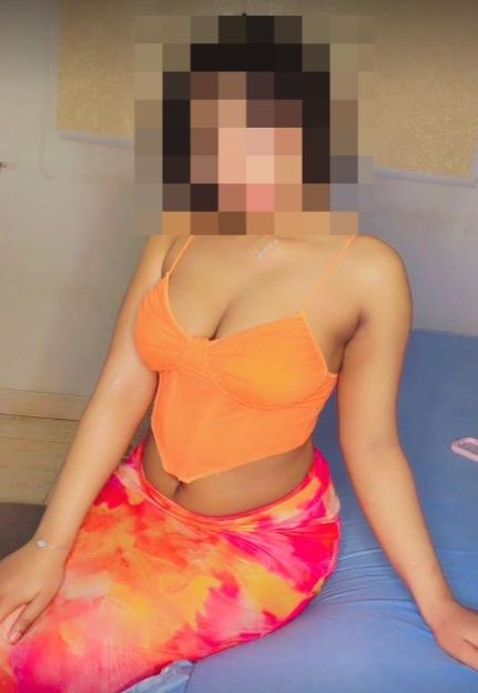 A woman in an orange top and a tie-dye skirt sitting on a blue bed.