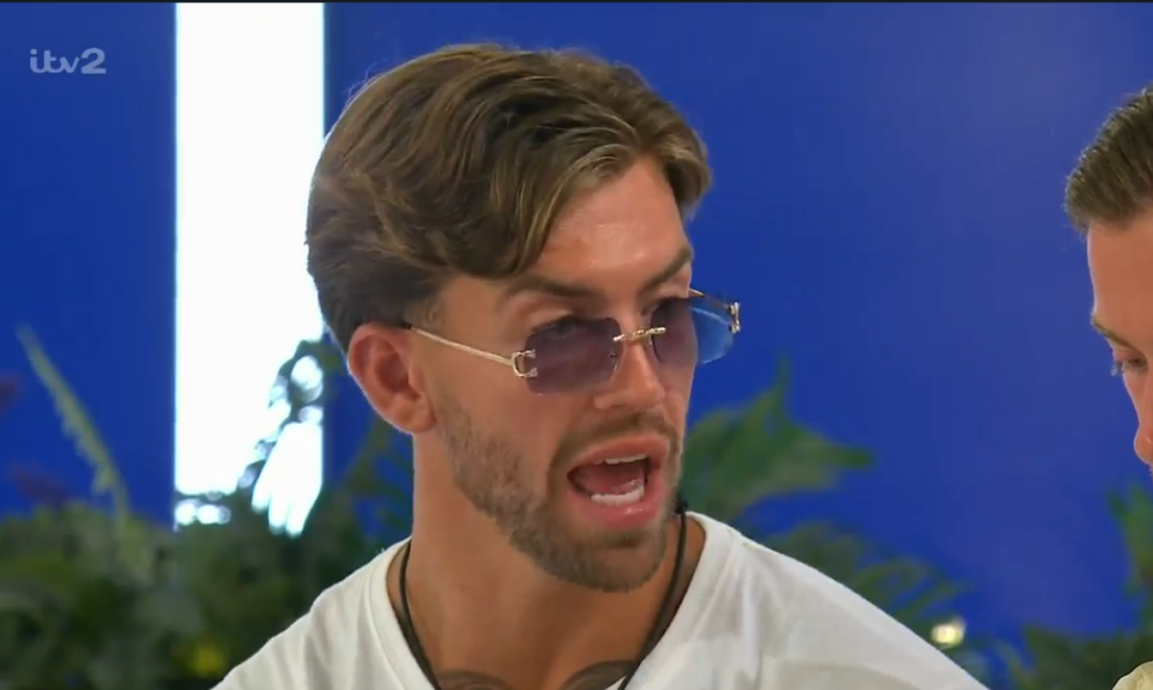 Man with light brown hair, sunglasses, and a white t-shirt talking.