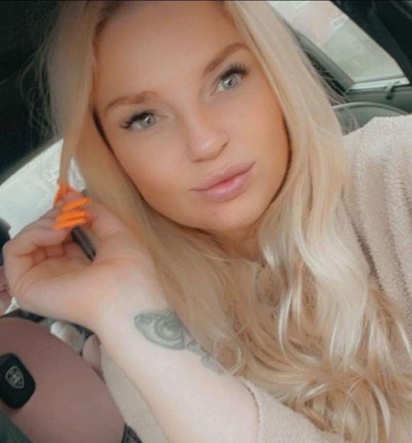 Jessica Lawson, a blonde woman, in a car wearing a peach-colored top, with bright orange fingernails and a tattoo of an eye on her wrist.