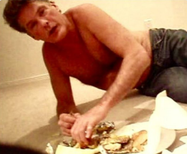 David Hasselhoff eating a cheeseburger on the floor, shirtless and wearing jeans.