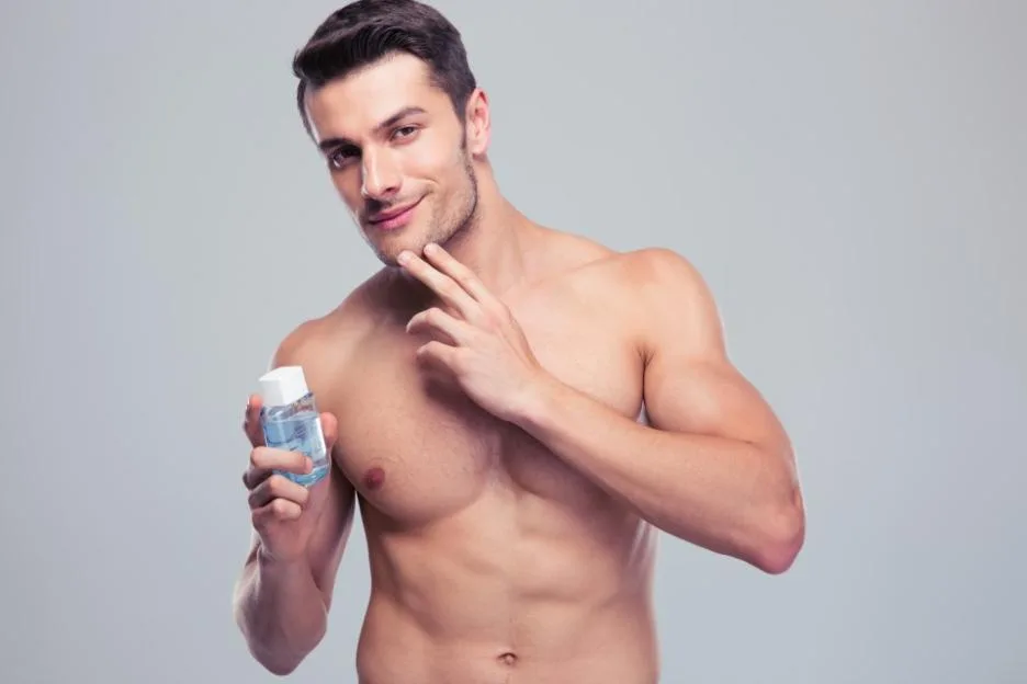 A shirtless man holding a bottle of lotion.