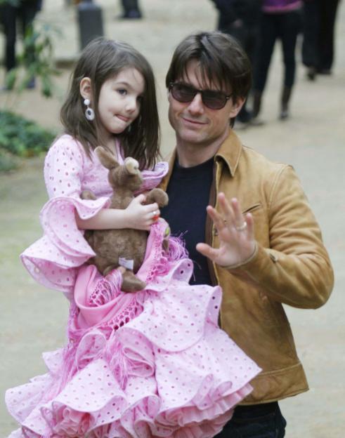 Tom Cruise holding Suri Cruise, who is wearing a pink dress and holding a toy.