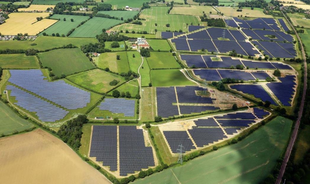 Aerial view of a sprawling solar farm in a rural area, with solar panels covering large sections of green and agricultural fields.