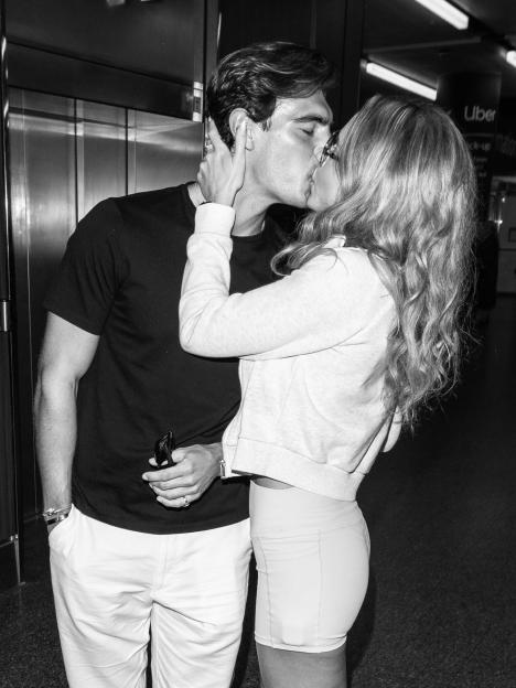 A man and woman kissing, the man with his eyes closed and the woman with sunglasses perched on her head.