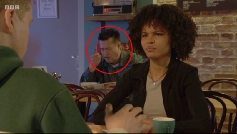 A man in a cafe in the background appears to be eating nothing with a fork.