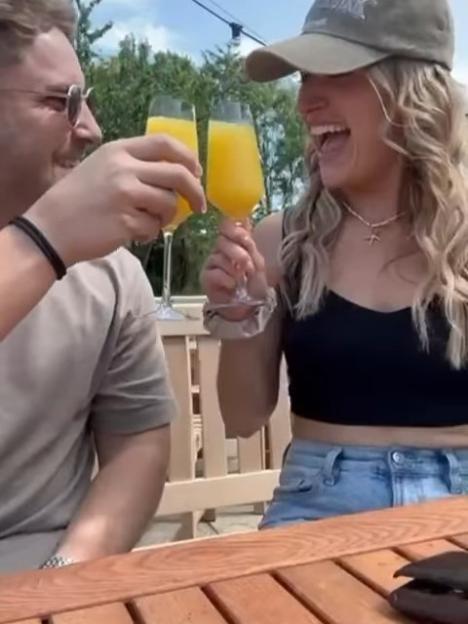 A man and woman clinking glasses of orange juice, laughing.