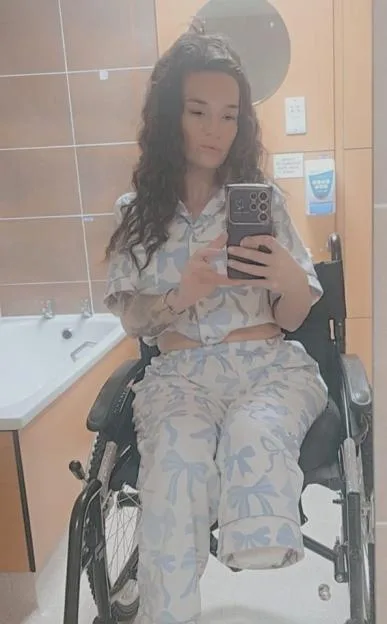 Danielle Thomas taking a mirror selfie in a wheelchair after a leg amputation.
