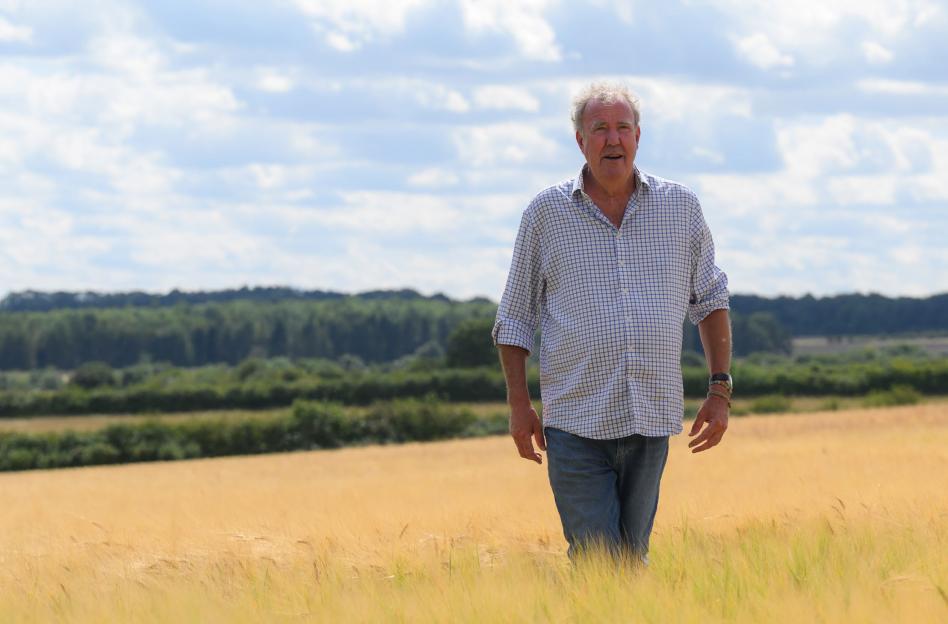 Jeremy Clarkson walking through a field of wheat under a cloudy sky.