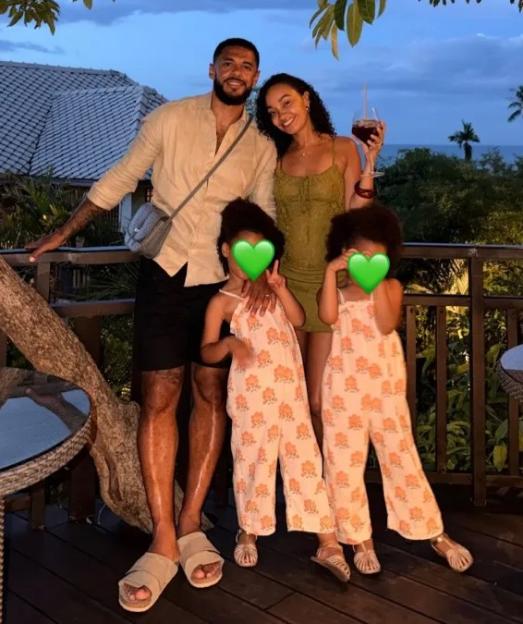 A family of four, including two young children with faces obscured, pose outdoors at dusk.