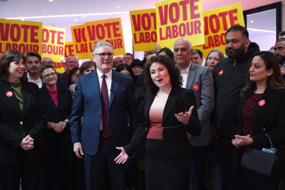 Keir Starmer and Lucy Powell look on as Angeliki Stogia speaks to a crowd, with "Vote Labour" signs visible in the background.