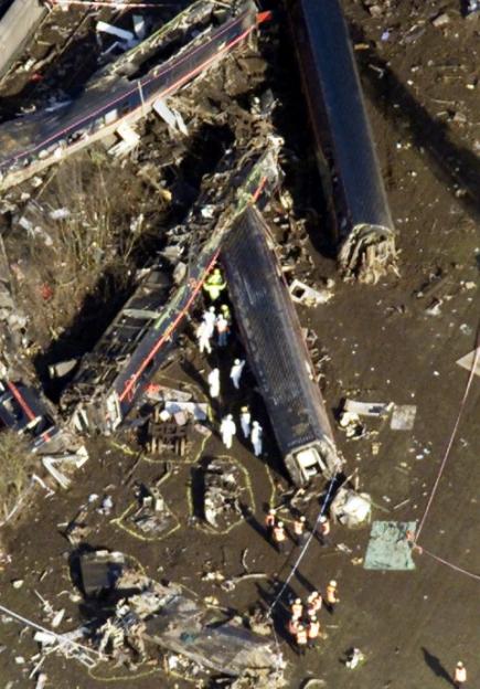 Aerial view of a train crash site with responders in white suits and orange vests.
