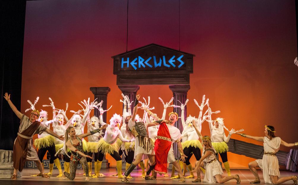 Actors in various costumes performing "Hercules" on stage.