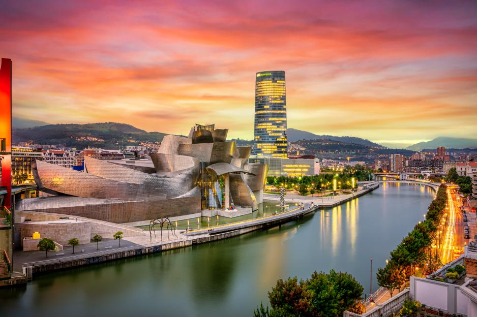 Cityscape of Bilbao at sunset with the Guggenheim Museum and Iberdrola Tower alongside the Nervion River.
