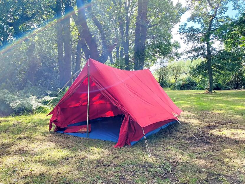 A red tent set up in a grassy, wooded area.