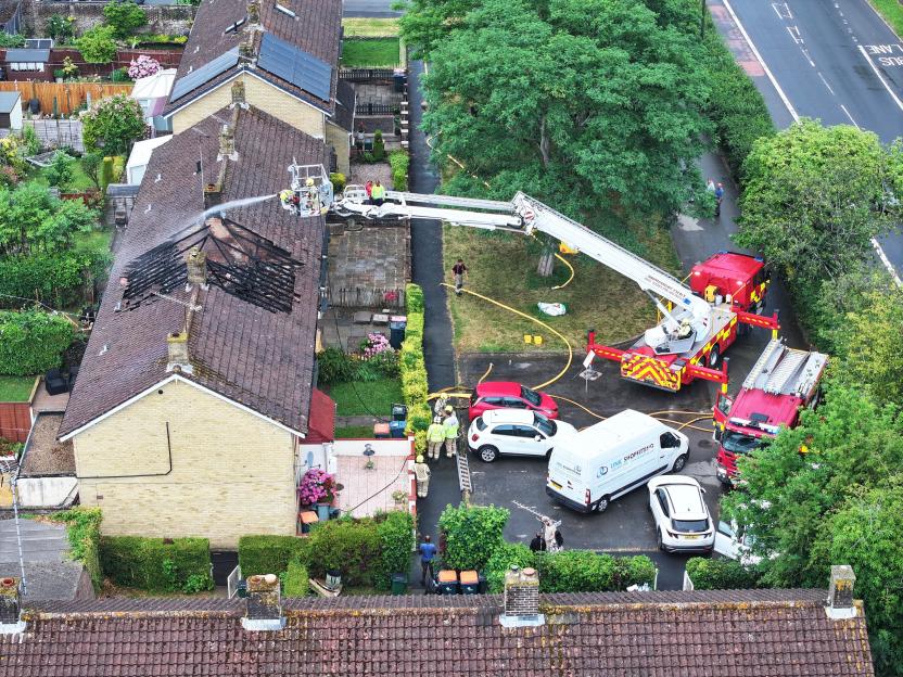 Firefighters in an aerial platform above a house with a collapsed and burnt roof.
